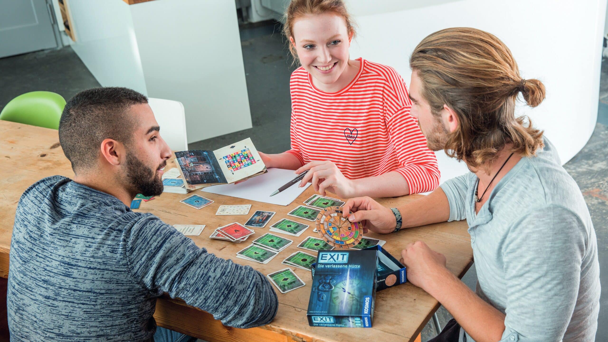 Tre amici si siedono a un tavolo e giocano al gioco EXIT La capanna abbandonata.