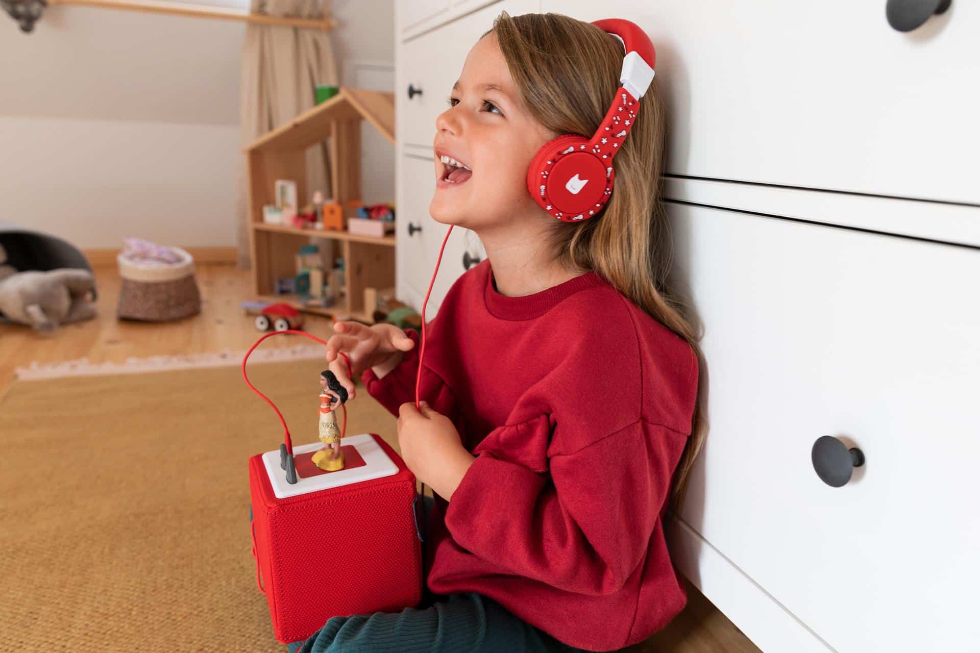 Una ragazza siede nella sua stanza e ascolta la musica con le cuffie del suo Toniebox.
